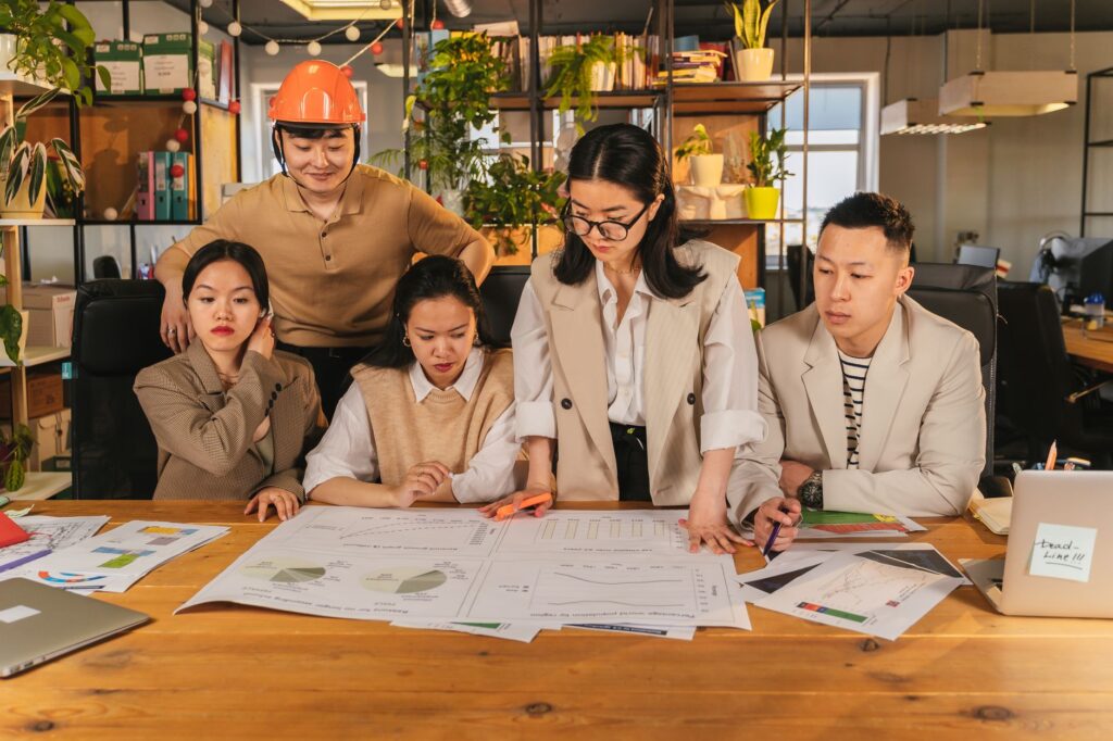 Diverse team collaborating on a project at a desk in a modern office environment with charts and plans.