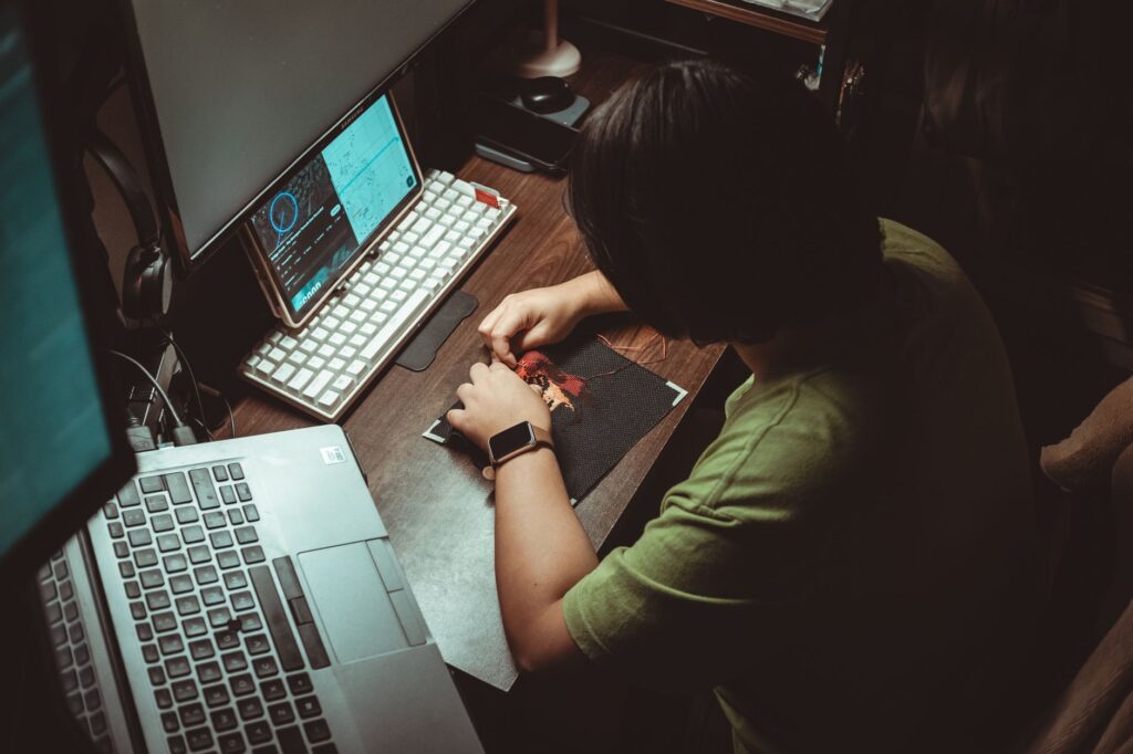 Person engaged in detailed artistic work at home office desk with technology tools.